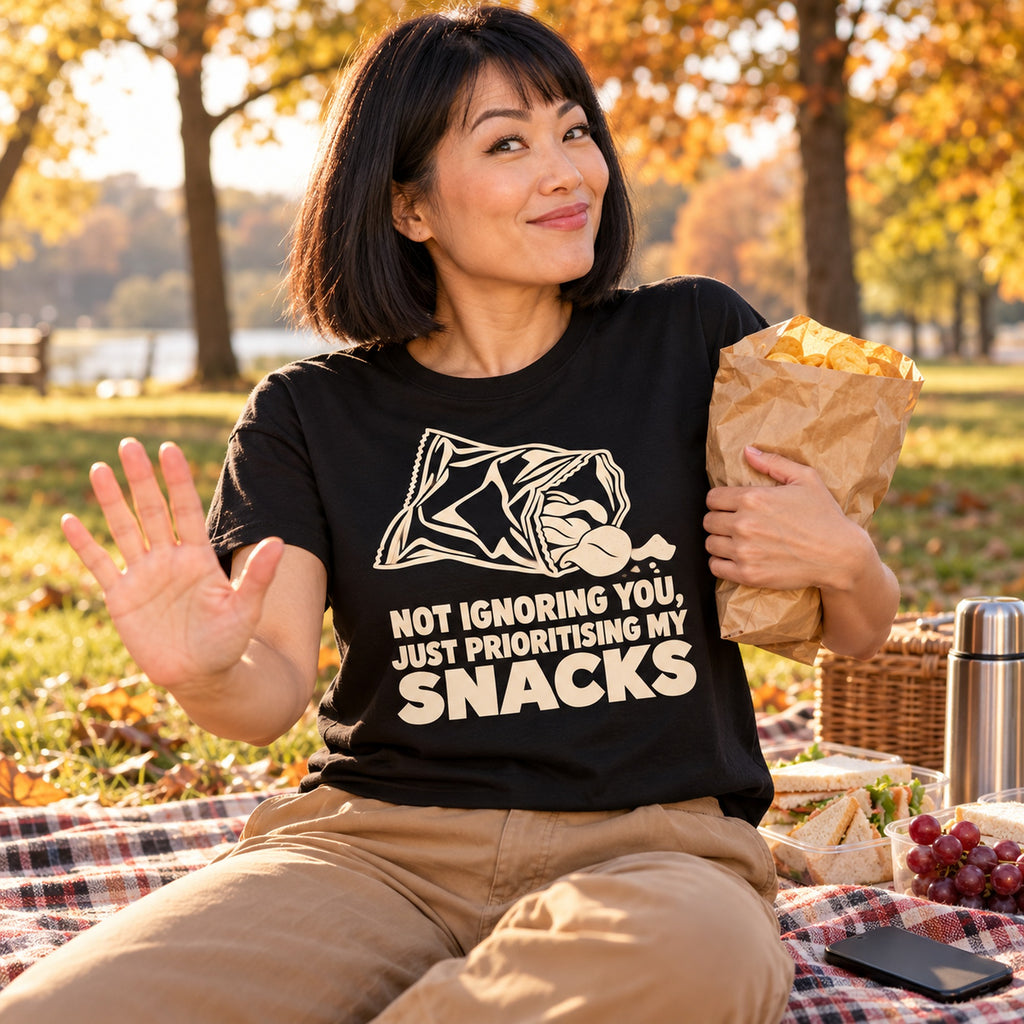 Woman wearing the Minimal Snack Bag design black t-shirt on a picnic blanket in an autumn park