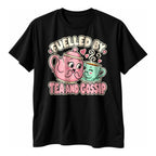 Black t-shirt with a pink teapot and a mint teacup whispering together above the text Fuelled By Tea And Gossip in cream and pink