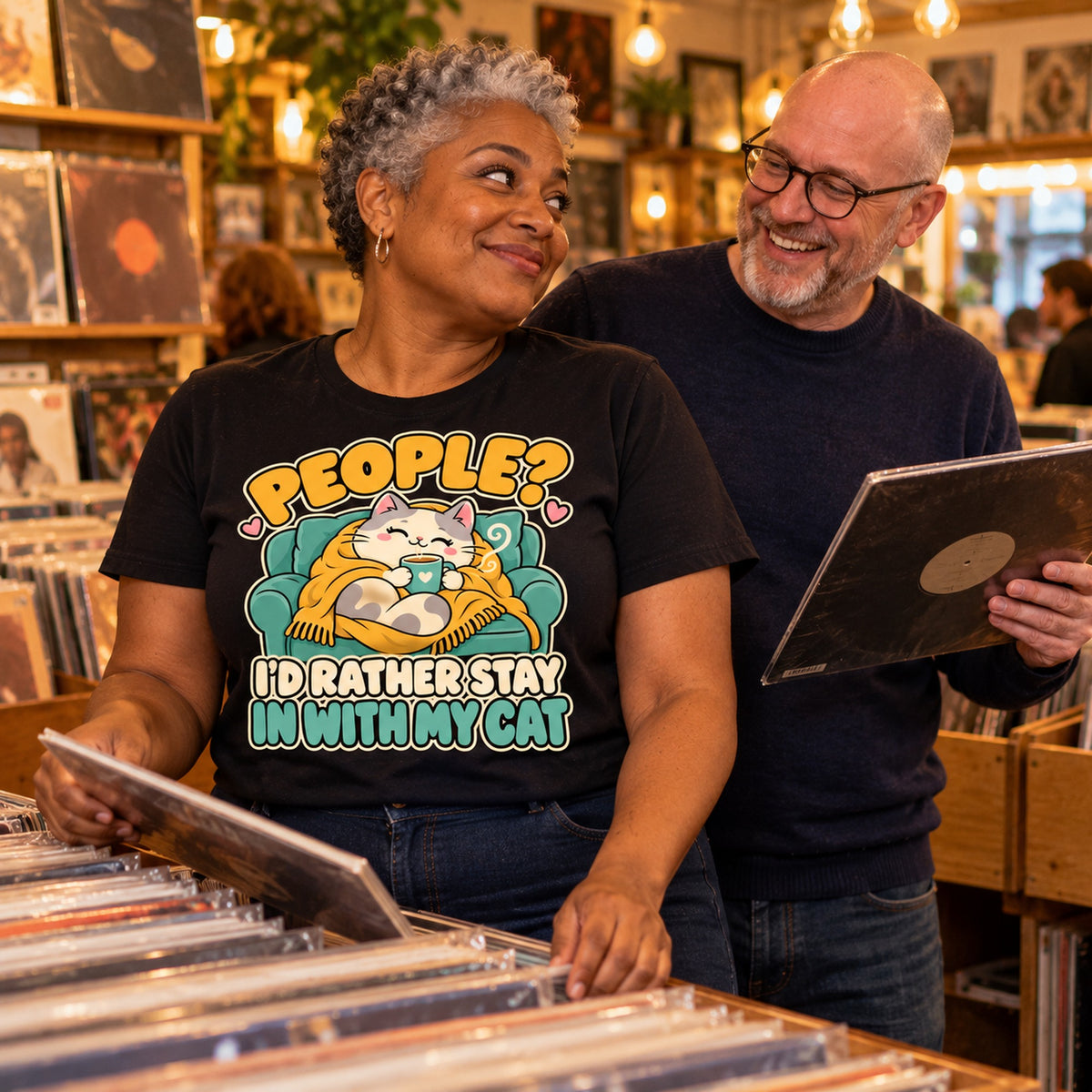 Couple in a vinyl record shop, woman wearing the Sofa Cat design black t-shirt