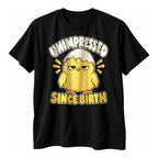 Black t-shirt with a fluffy yellow chick wearing half an eggshell as a hat above the text Unimpressed Since Birth
