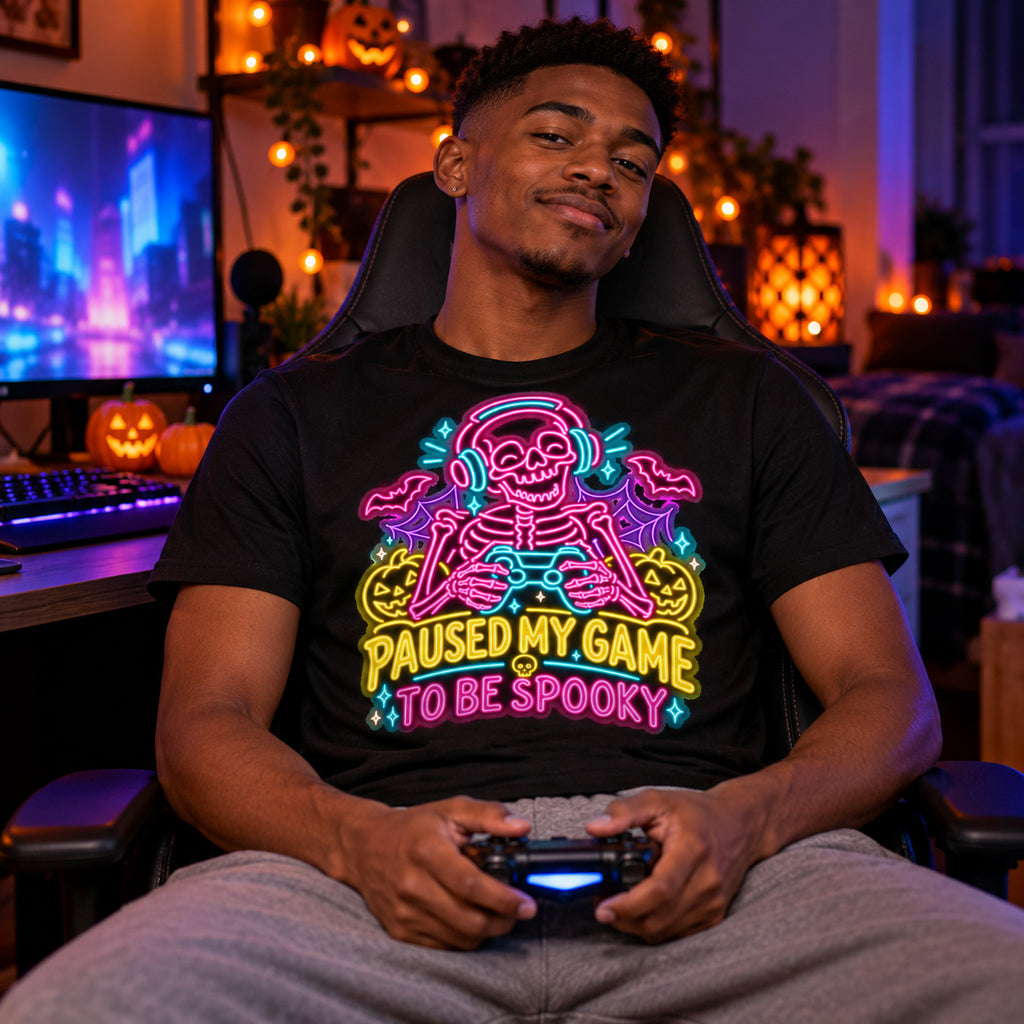 Man wearing the Neon Skeleton Gamer design black t-shirt at a gaming desk in a bedroom with Halloween lights