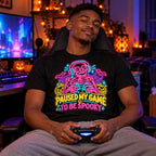 Man wearing the Neon Skeleton Gamer design black t-shirt at a gaming desk in a bedroom with Halloween lights