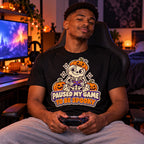 Man wearing the Sticker Skeleton Gamer design black t-shirt at a gaming desk in a bedroom with Halloween lights