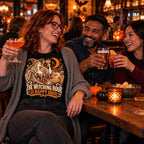Colleagues wearing the Woodcut Witch Toast design black t-shirt toasting drinks at a pub table with small pumpkins