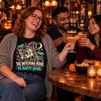 Colleagues wearing the Doodle Witch Happy Hour design black t-shirt toasting drinks at a pub table with small pumpkins