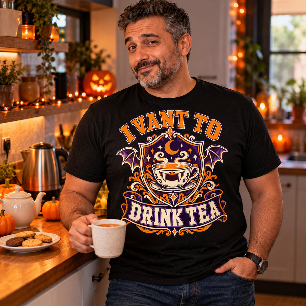 Man wearing the Varsity Tea Crest design black t-shirt holding a mug of tea in a kitchen with Halloween pumpkins