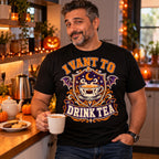 Man wearing the Varsity Tea Crest design black t-shirt holding a mug of tea in a kitchen with Halloween pumpkins