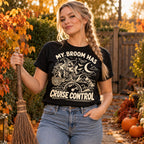 Woman wearing the Line Art Autopilot Witch design black t-shirt holding a straw broom in an autumn garden with pumpkins