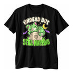 Black t-shirt with a cartoon green zombie cat asleep on a tombstone above the text Undead But Still Napping
