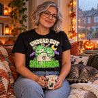 Woman wearing the Cartoon Zombie Cat Tombstone design black t-shirt on a cosy window seat with a sleeping cat