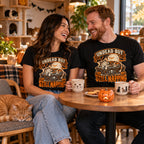 Couple wearing the Woodcut Coffin Cat design black t-shirts at a cat cafe table with a ginger cat napping