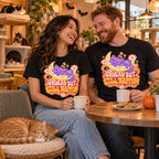Couple wearing the Groovy Moon Cat design black t-shirts at a cat cafe table with a ginger cat napping