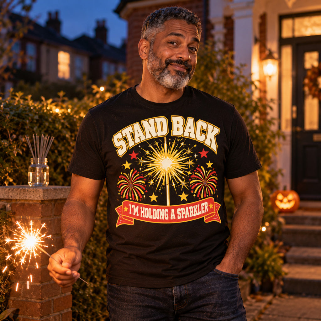 Man wearing the Varsity Sparkler Star design black t-shirt on his front garden path at dusk holding a sparkler