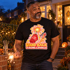Man wearing the Sticker Mitten Sparkler design black t-shirt on his front garden path at dusk holding a sparkler