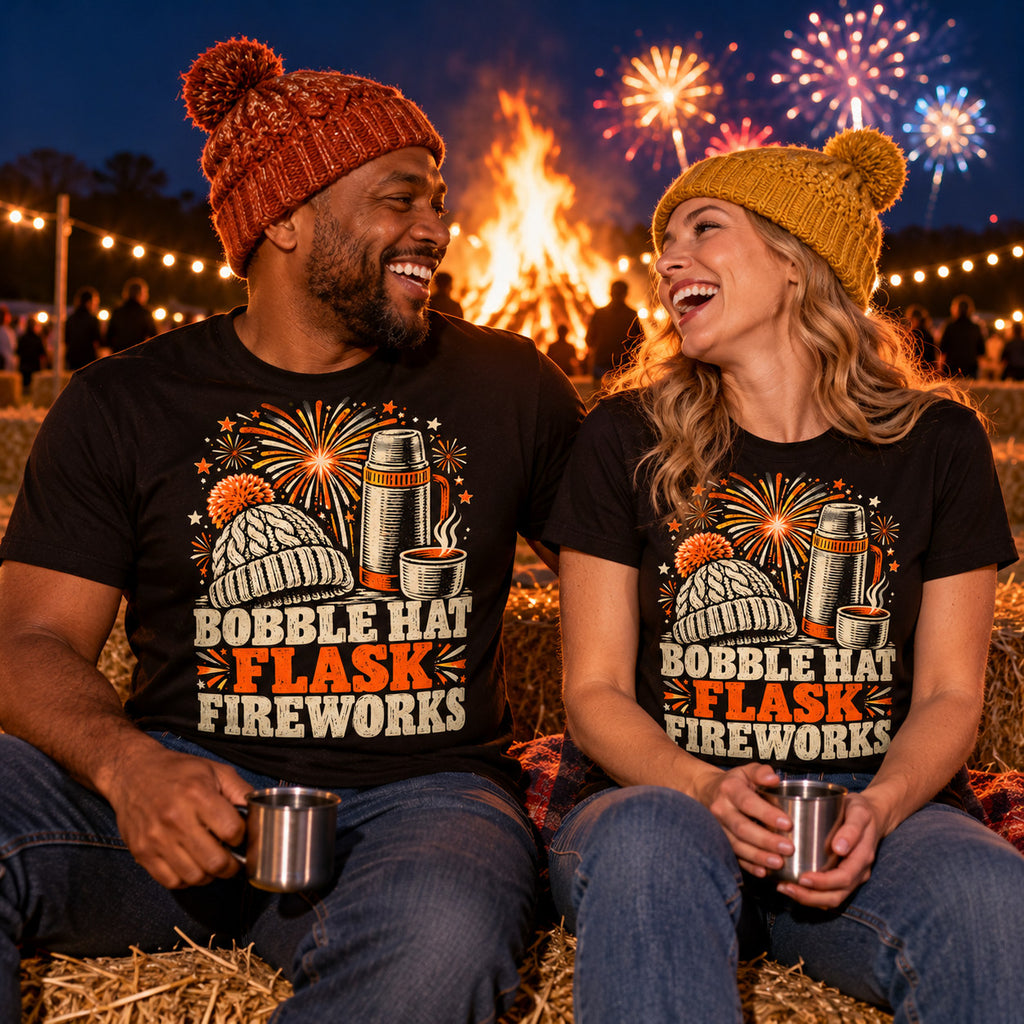 Couple wearing matching Woodcut Kit Trio design black t-shirts on straw bales by a bonfire sharing a hot drink