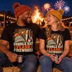 Couple wearing matching Woodcut Kit Trio design black t-shirts on straw bales by a bonfire sharing a hot drink