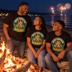 Family wearing matching Campfire Badge design black t-shirts by a driftwood bonfire on a pebble beach at night