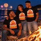 Family wearing matching Sticker Campfire design black t-shirts by a driftwood bonfire on a pebble beach at night