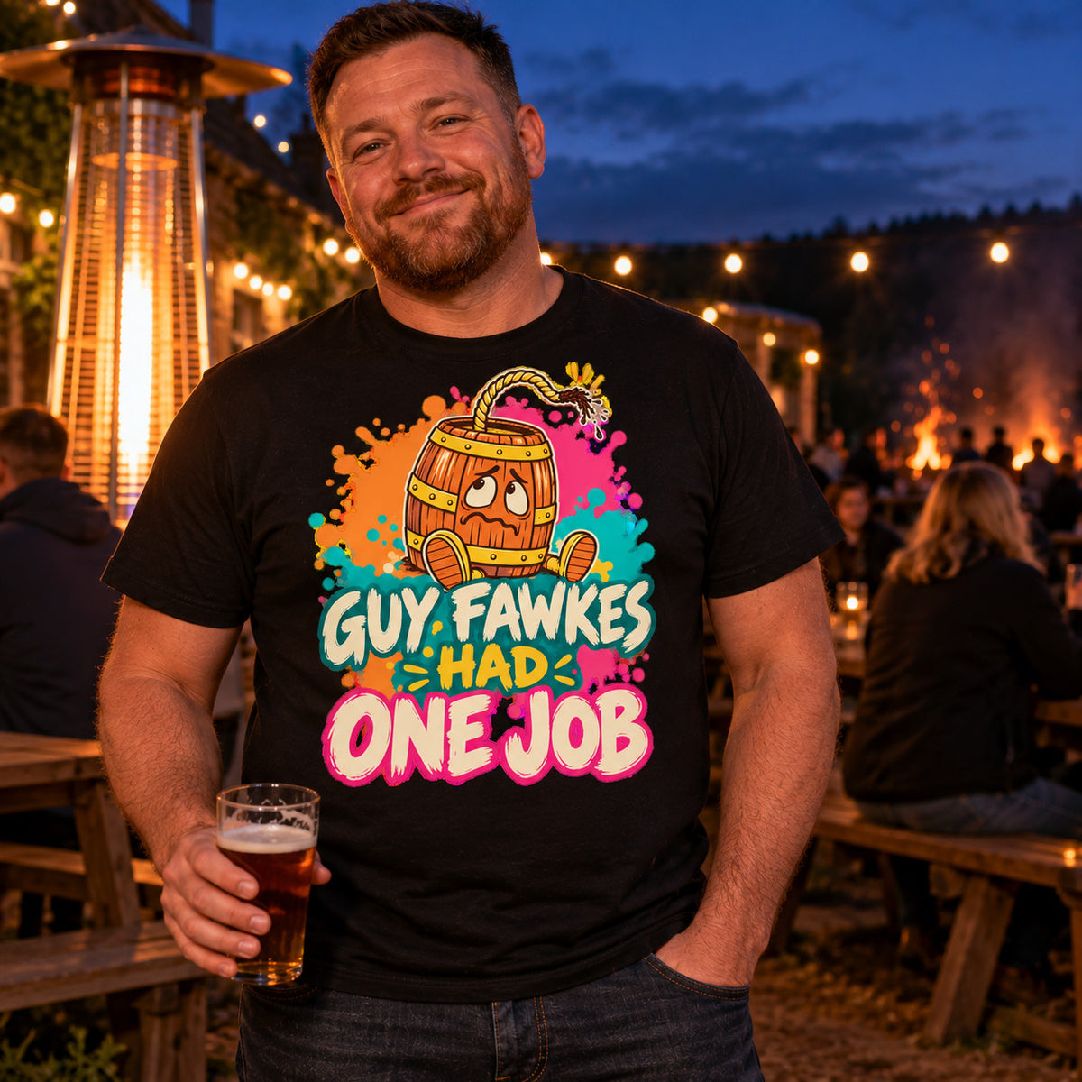 Man wearing the Splash Barrel design black t-shirt in a pub beer garden at dusk holding a pint with a bonfire glowing behind