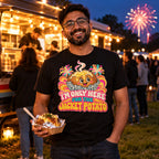 Man wearing the Groovy Spud design black t-shirt at a park street food van at dusk holding a foil wrapped jacket potato with fireworks behind