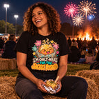 Woman wearing the Badge Spud design black t-shirt sitting on a hay bale at a school field fireworks night holding a foil wrapped jacket potato