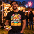 Man wearing the Doodle Spud design black t-shirt at a park street food van at dusk holding a foil wrapped jacket potato with fireworks behind