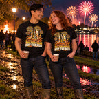Couple wearing matching Woodcut Wellies design black t-shirts and wellington boots in a muddy riverside park at a fireworks night holding hot chocolates