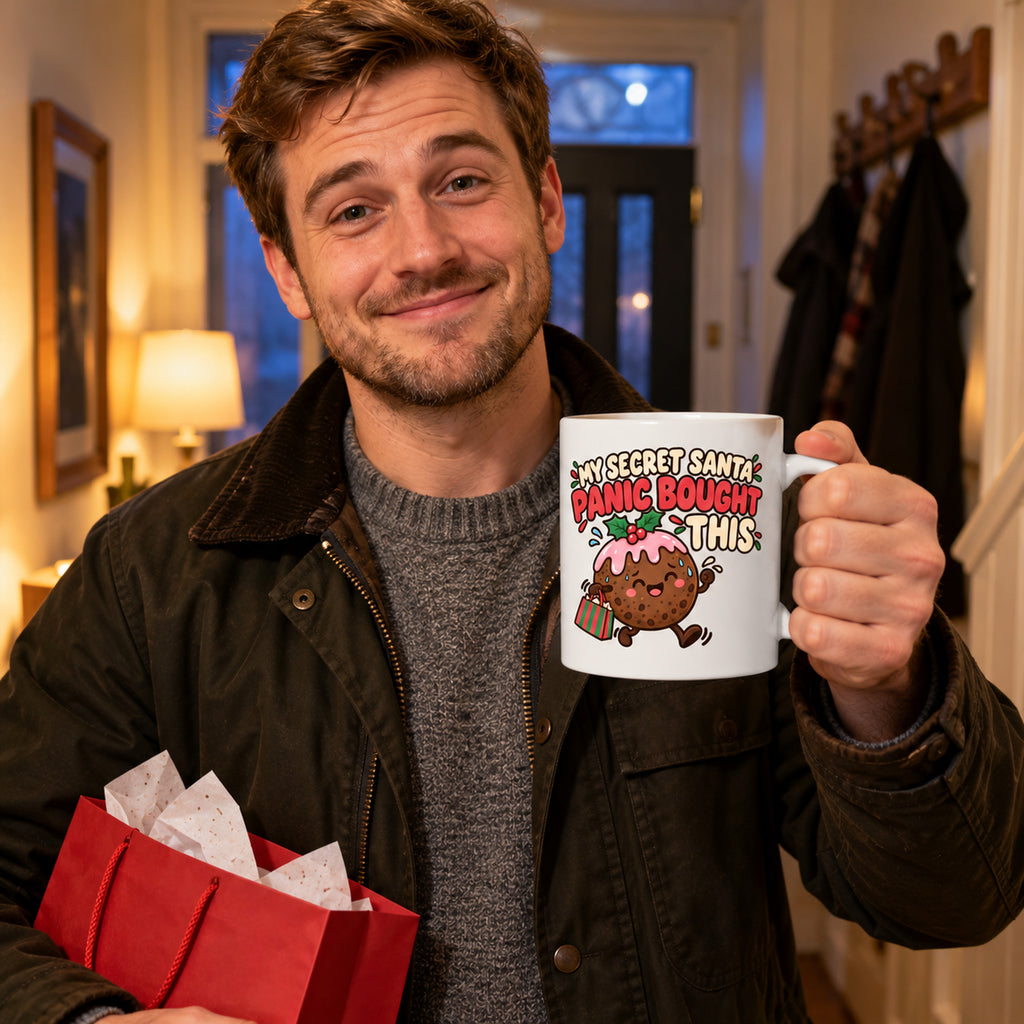 White mug with a smiling Christmas pudding carrying a bag under the words My Secret Santa Panic Bought This, lifestyle photo 1