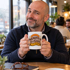 White mug with wavy brown lettering, rainbow arcs, daisies and a banner reading Working With You Was A Pleasure, Mostly, lifestyle photo 1